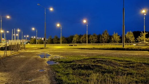 Miasto w świetle latarni, droga szutrowa z kałużami. Miasto po deszczu, nocą.